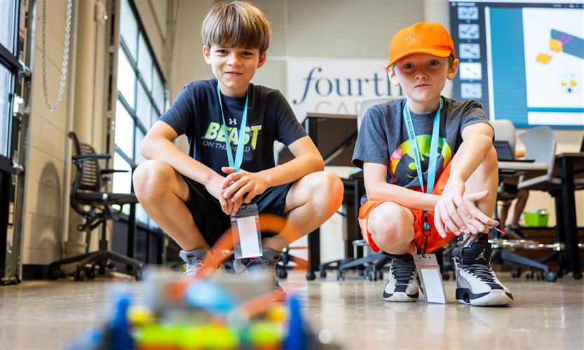 Two boys watch a robot on the ground